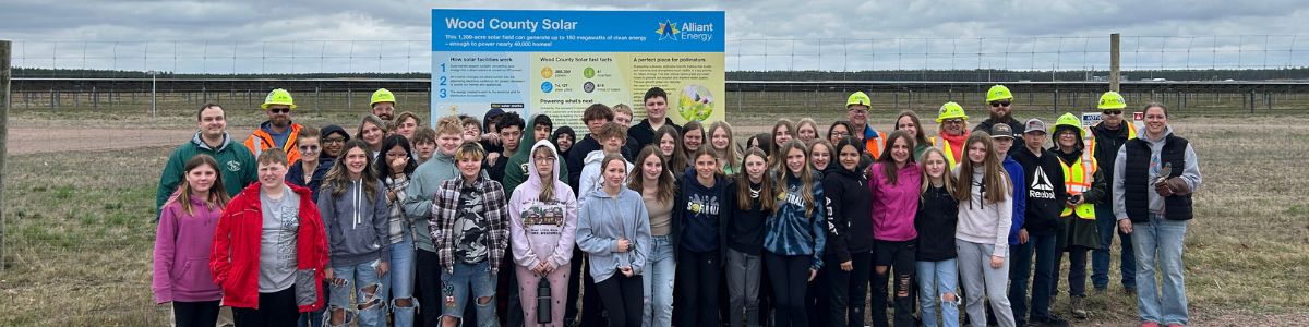 Middle school students, Alliant Energy employees wearing hard hats and a kestrel handler holding a kestrel at Wood County Solar.