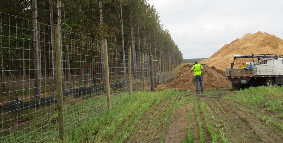 Crews install an 8-foot woven wire fence around the boundary of the project site to keep large animals away. (Oct. 8, 2021)