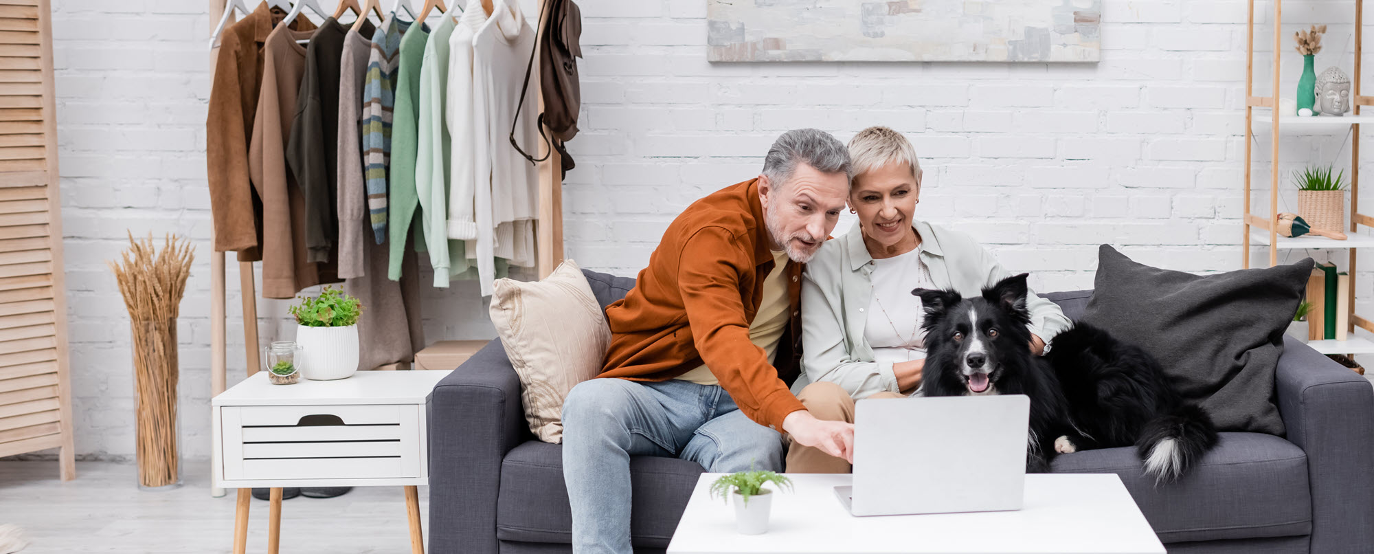 couple on a couch with their dog. looking at a laptop