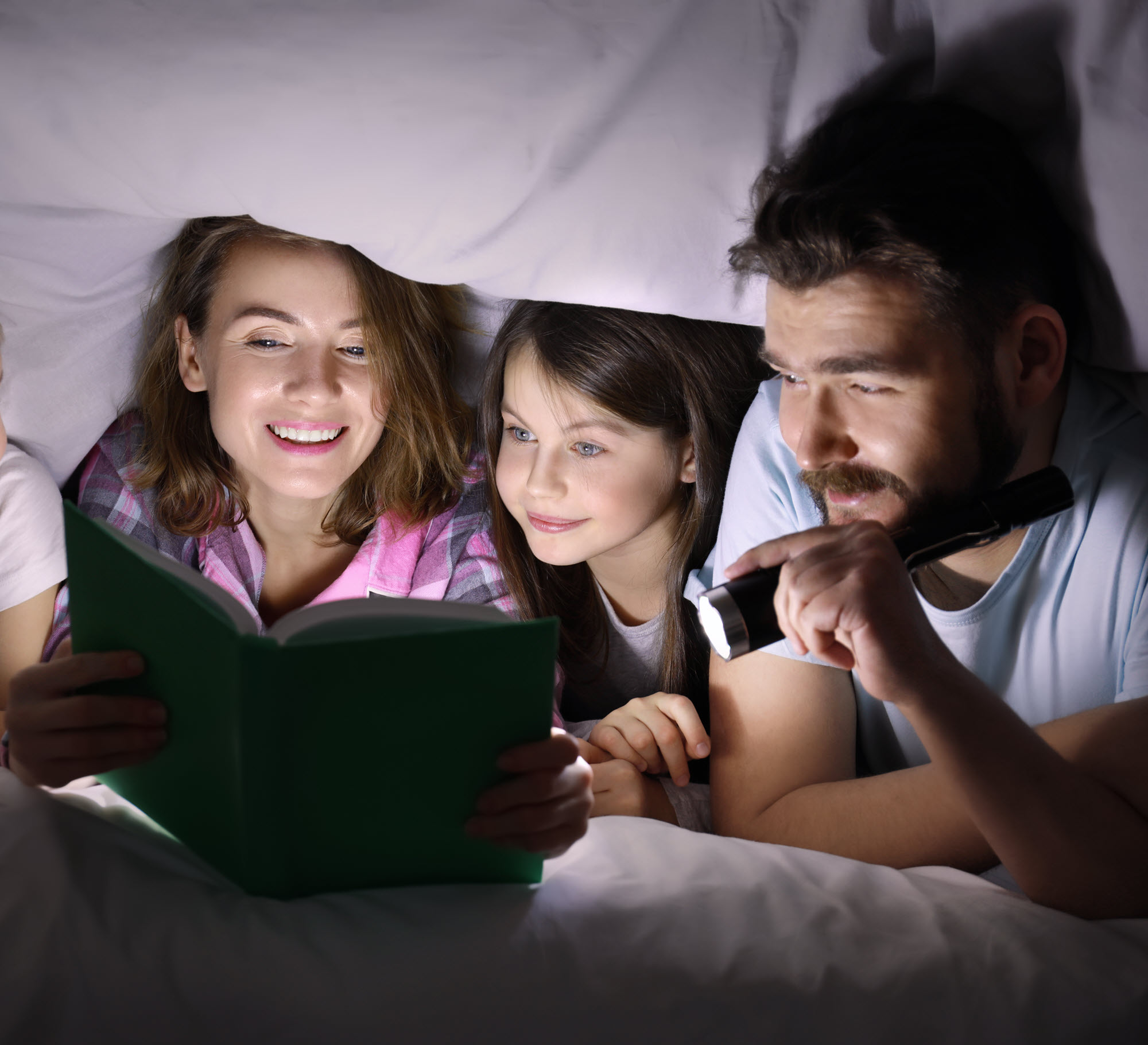 family in a blanket fort reading a book by flashlight