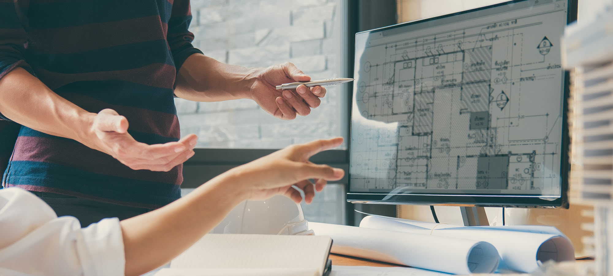Two people at work looking at blueprints on a computer screen
