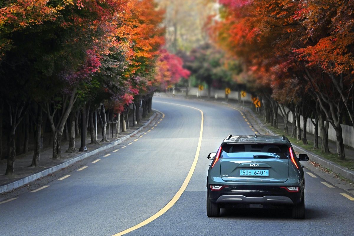 Electric vehicle driving down a road lined with trees in the fall. 