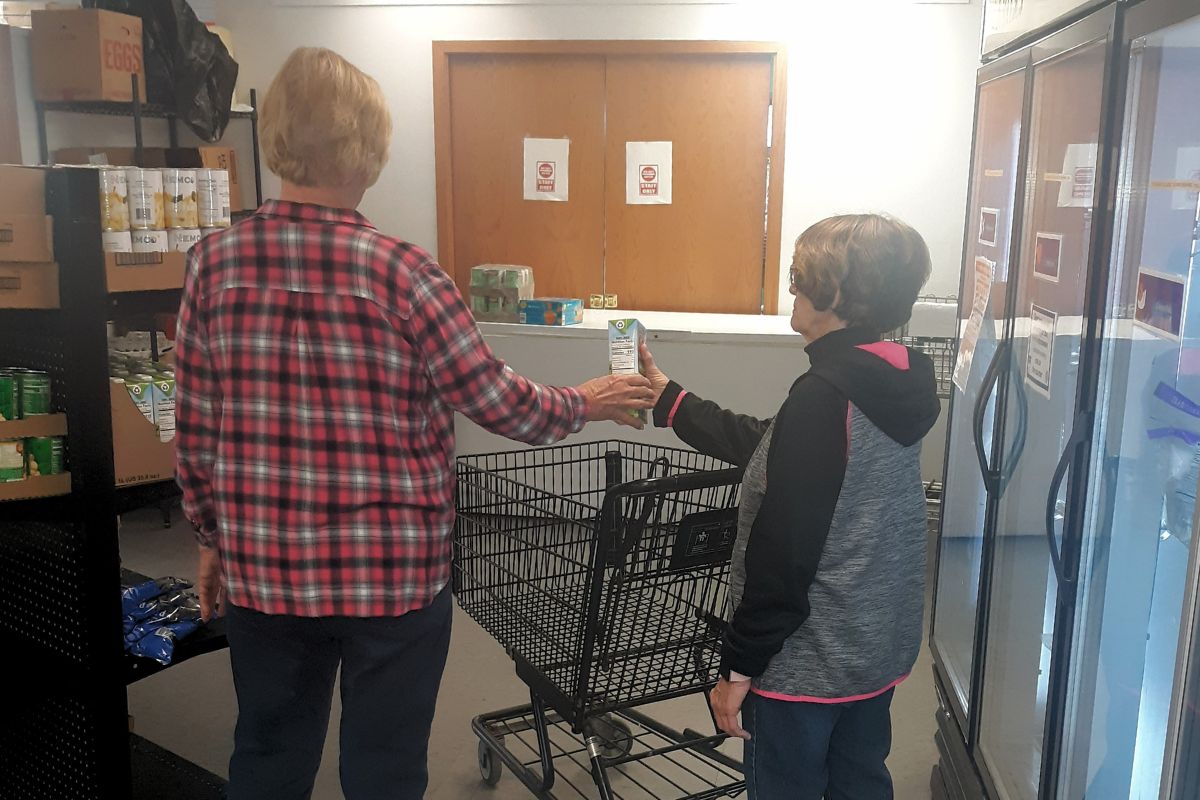 A shopper handing another shopper a can to put in their cart at a food pantry. 