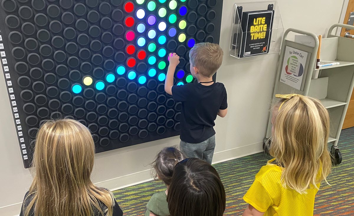 Kids playing with a large interactive Lite Brite on a wall