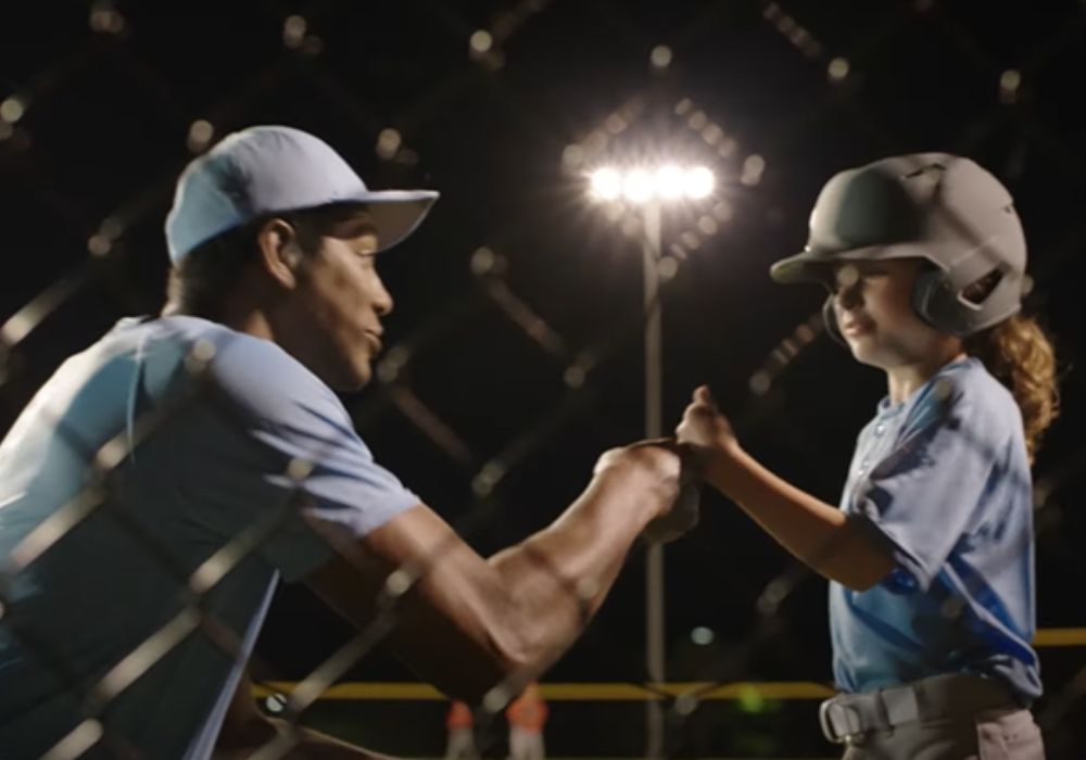 Young girl and coach fist bumping on baseball field