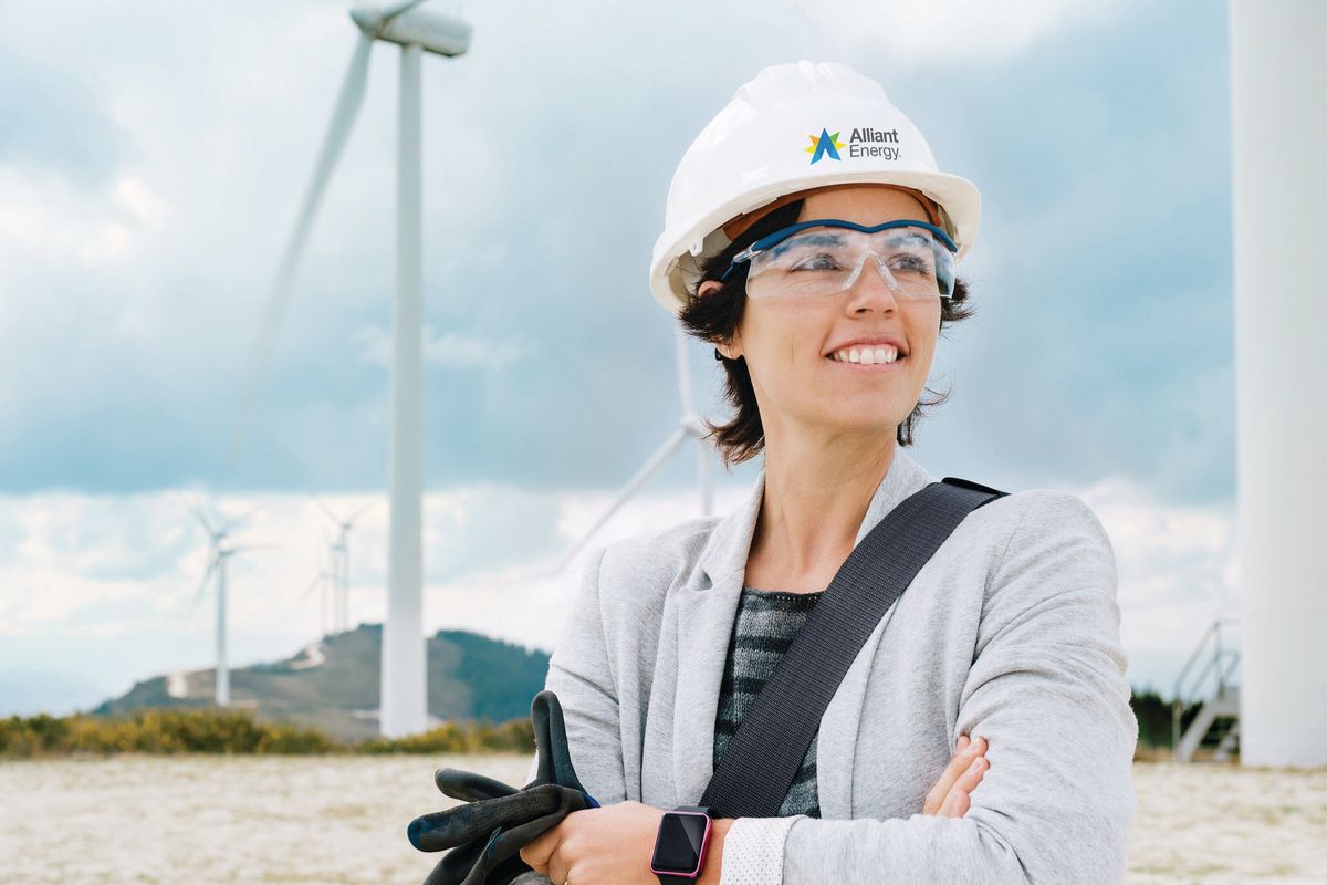 Woman wearing a hard hat and safety goggles standing in front of wind turbines. 