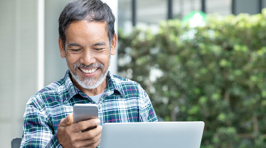 Older person outside with laptop smiling at phone