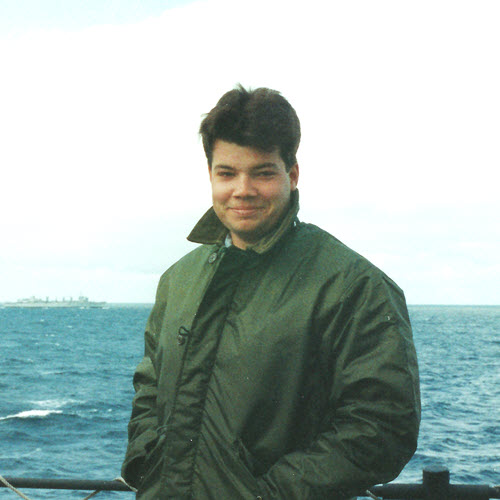 man standing near water with a military boat in the water