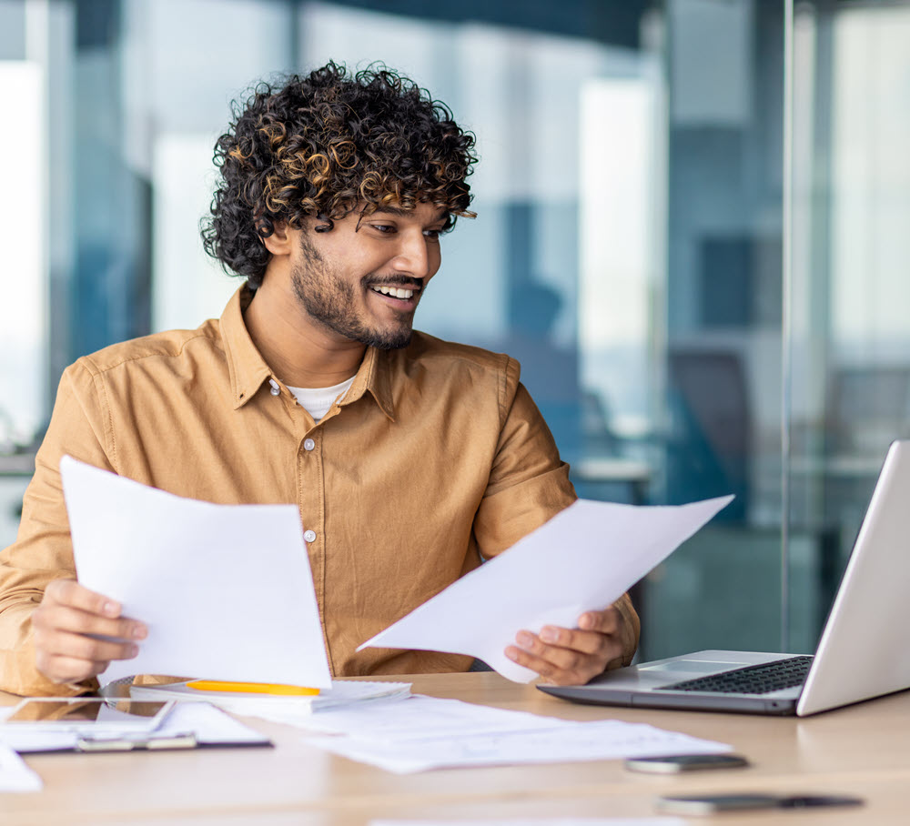 man in office with paperwork and laptop