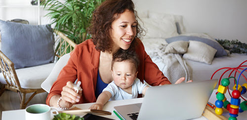 mom holding a baby and working on a laptop