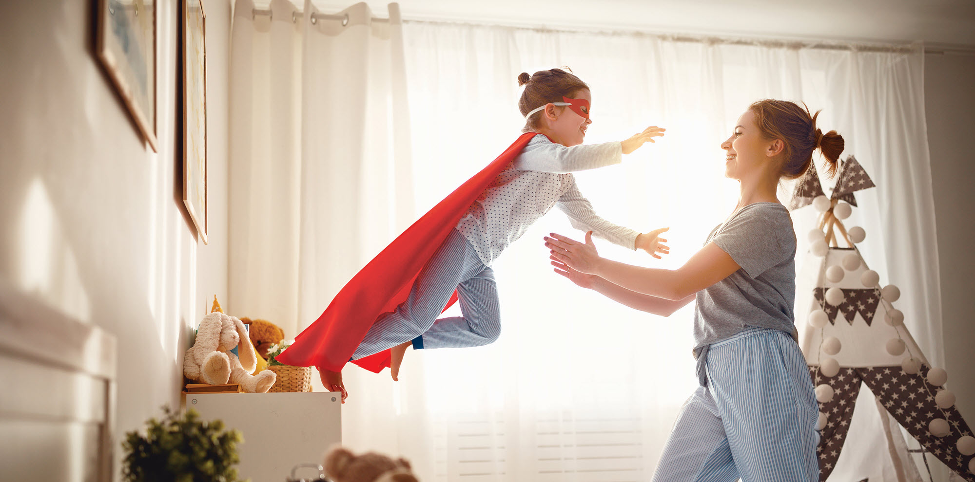 girl in a superhero costume leaping toward her mom